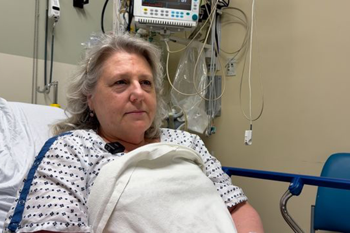 Woman with graying hair sitting up on a gurney/exam table in a hospital setting. 